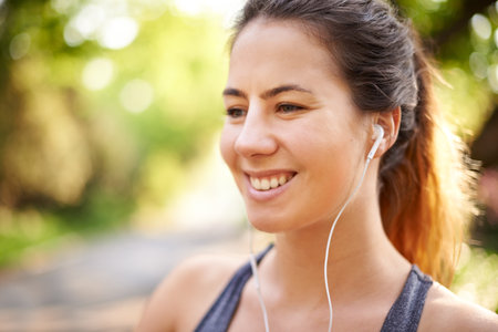 Runner, smile and woman with music at park for cardio break, running podcast or fitness sound. Space, female athlete and earphones in nature for exercise, listening to radio or thinking of workoutの写真素材