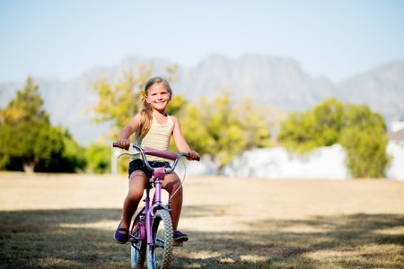 Girl, child portrait and outdoor for riding bicycle, learning development and practice in neighborhood. Happy, bike and female person for travel adventure on weekend, kid and holiday for childhoodの写真素材