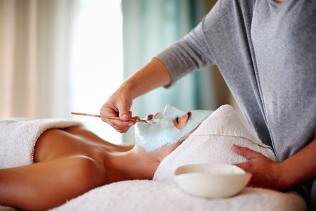 Beauty, hands and client with mask at spa for facial treatment, deep cleaning or skin exfoliation. Skincare, beautician or woman with clay application for hydration or natural glow at wellness salonの写真素材