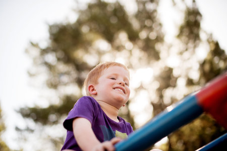 Merry go round, play and smile of boy outdoor in nature for child development, growth or having fun. Balance, happy and youth with excited kid on carousel from below for playground adventureの写真素材