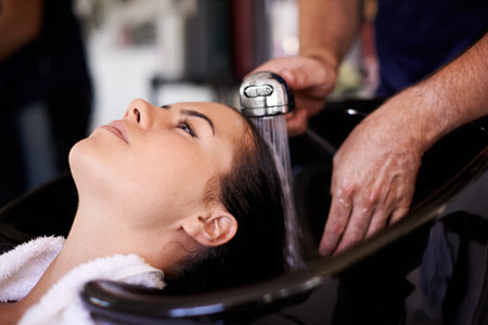 Woman, hairdresser and shower in salon with water, basin and cleaning for hygiene, routine and wellness. People, service and washing for hair care with helping hand for cosmetics, change and growthの写真素材