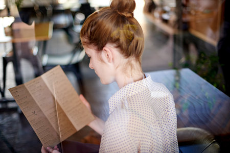Cafe, woman and reading with menu, food decision or beverage choice. Girl, back and lunch with options of restaurant for hunger, snack or meal at coffee shop or bistro for hungry customer orderの写真素材