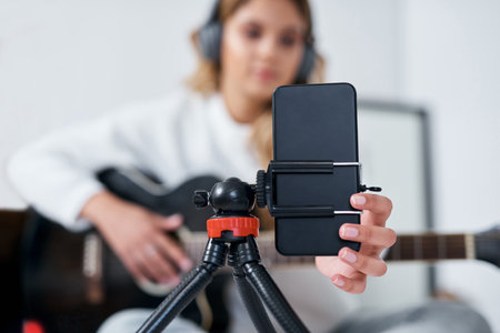 Hands, phone and guitar in home, recording and video with social media for album promotion in bedroom. Person, artist and musician with content creation, instrument and live stream performance on webの写真素材