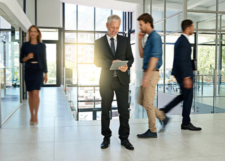 Business people, walking and man on tablet in office for productivity, synergy and coworking. Professional, corporate workers and mature person in busy workplace for movement, rush and hurry in lobbyの写真素材