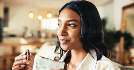 Thinking, woman and eating chocolate candy in home, comfort food and hungry for sugar snack. Delicious, sweets and person with dark cacao treat for confectionery dessert, idea or relax in living roomの写真素材