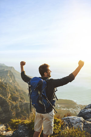 Happy, man and hiking with success on mountain of travel celebration, nature freedom and achievement. Male person, cheering and trekking victory for fitness adventure, climbing challenge and locationの写真素材