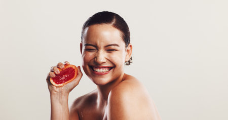 Happy woman, grapefruit or squeeze with vitamin C for skincare, detox or nutrition on a white studio background. Female person, model or smile with natural organic fruit for antioxidant on spaceの写真素材