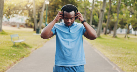 Headphones, music or black man in park for running, training exercise or workout for fitness. Outdoor, African athlete and healthy male runner listening to sports podcast, motivation or radio audioの写真素材