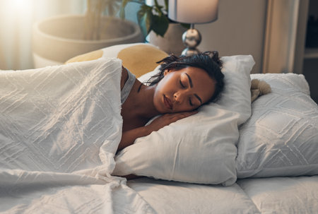 Woman, tired and sleeping in bed for relax, comfort and exhausted in home with blanket and pillow. Female person, fatigue and asleep in bedroom for nap, dream and burnout with rest, peace and breakの写真素材