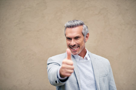 Portrait, smile and thumbs up with business man on wall background for motivation, support or thank you. Bonus, promotion and success with happy mature employee on mockup space for emoji, like or yesの写真素材