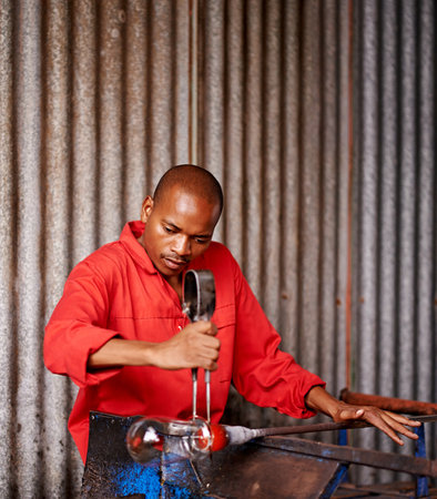 Glass blowing, artist and black man in workshop for creative small business, craft and handmade shape. Art, product process and glassblower in factory for sustainable project, design and heat toolsの写真素材