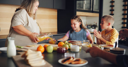 Mother, children and serving breakfast in kitchen with healthy food, pouring juice and eating together. Happy family, woman and kids with lunch meal in home for wellness, hunger support and bondingの写真素材