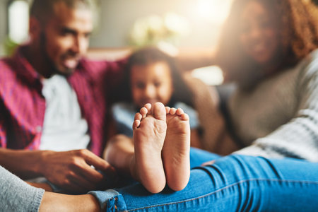 Feet, family and relax in living room, home and parents with child, group and comfortable in socks. House, legs and people in lounge with kid, mom and dad with youth on couch, bonding and chillingの写真素材