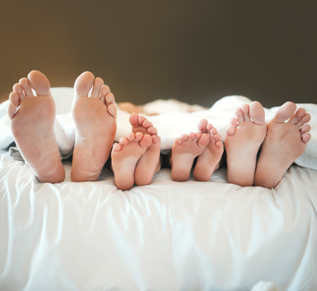 Feet, relax and sleeping with family in bed together for morning or weekend recovery and rest. Blanket, comfortable or dreaming with mother, father and sibling children in apartment for bondingの写真素材