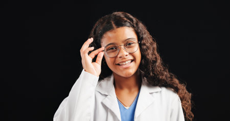 Portrait, child and doctor with glasses in studio for future career, playful learning and medical costume. Smile, kid and eyewear for healthcare fantasy, education and opportunity on black backgroundの写真素材