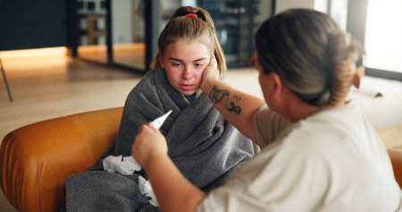 Sick girl, mom or fever with thermometer on sofa for illness, influenza or virus at home. Teenager, mother and daughter with checkup or temperature for viral infection, healthcare or results at houseの写真素材