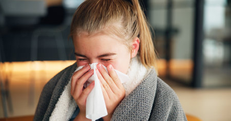 Sick girl, cold and blowing nose with tissue for influenza, flu or viral infection at home. Child, kid or teenager with sneeze, sinus or hayfever for virus, allergy or illness from contagious diseaseの写真素材