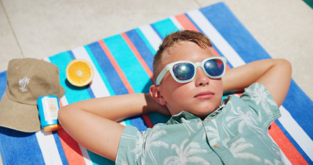 Tanning, sunglasses and boy on towel for outdoor holiday, travel and vacation to relax or chill. Above, tropical and male kid sunbathing in summer at lodge, hotel and resort on weekend break in Miamiの写真素材