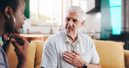 Mature man, nurse and stethoscope for checkup of cardiology, medical service and healthcare advice. Caregiver, patient and explaining symptoms for consultation, monitor breathe and treatment at houseの写真素材