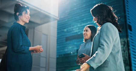 City, women and smile for discussion, business and real estate agent with clients and conversation. Outdoor, employee and opportunity for investment for company, lens flare and corporate peopleの写真素材