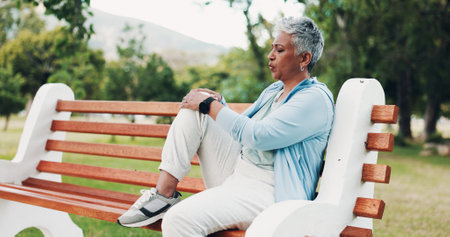 Knee pain, fitness and mature woman in park with injury, muscle strain and inflammation on bench. Nature, sports and senior person with accident for exercise, workout and walking outdoors for healthの写真素材