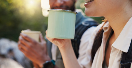 Mug, coffee and hiking with interracial couple in nature for lunch break, trekking adventure and park conservation. Drinking, conversation and environment with closeup of man and woman in forestの写真素材