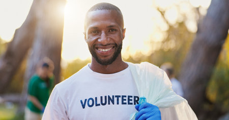 Portrait, volunteer and happy man with trash bag outdoor for cleaning, community service or pollution. Garbage, charity worker and park for environment care, recycling or waste management at sunsetの写真素材