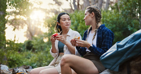 Picnic, food and hiking with friends in nature for lunch break, trekking adventure and park travel. Eating, conversation and environment with women in forest for snack, relax and peace togetherの写真素材