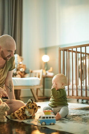 Man playing with tired baby on nursery floor, new dad and infant bonding with toys in bedroom at home. Family, love and development, father and child in playroom, teaching and learning with fun toy.の写真素材
