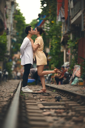 Love, kiss and couple on train tracks in Vietnam for holiday, vacation and tourist destination. Embrace, weekend and man and woman on railway for adventure, journey and travel for bonding in cityの写真素材