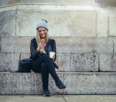 Coffee, city or happy woman on steps with mobile app on social media, internet or blogging for fashion tips. Urban town, beverage or trendy girl online to search cool clothes with phone or textingの写真素材