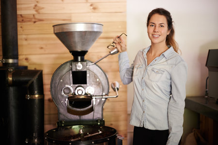 Coffee machine, roast and portrait with happy barista woman in kitchen of restaurant for brewing or hospitality. Caffeine, equipment and smile with waitress in cafe for retail sale of fresh beverageの写真素材