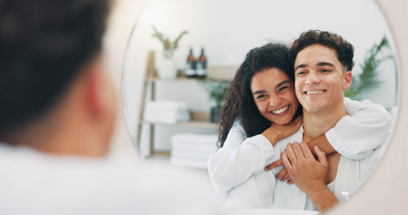 Happy couple, mirror and bathroom with hug for hygiene, skincare or morning routine together at home. Man, woman or lovers with smile, reflection or embrace for grooming, love or spa day at houseの写真素材
