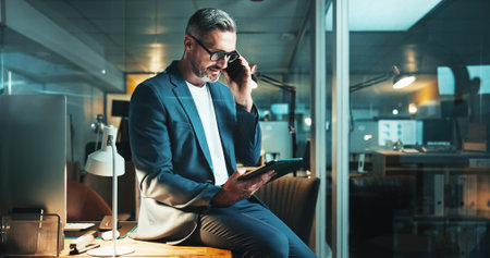 Mature man, tablet and phone call with office, overtime work or project feedback. Web design, night or email update for programmer, cloud computing and research negotiation or online communicationの写真素材