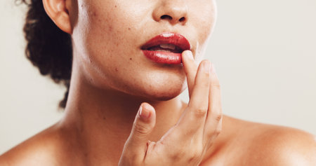 Lips, shine and makeup with hand of woman in studio for beauty product, self care and cosmetics. Closeup, aesthetic and salon with person on white background for glow, spa treatment and mouthの写真素材