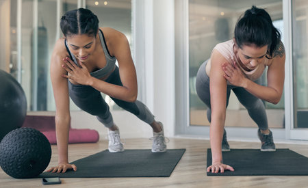 Fitness, balance and women in gym, training and strength for exercise with personal trainer and plank. Together, people and workout for core muscles, stability and wellness with instructor in classの写真素材