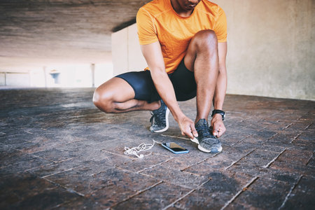 Fitness, shoes and tying laces with man in city for workout challenge, tracking time and running. Phone, marathon practice and health app with person in parking lot for sneakers, training and sportの写真素材