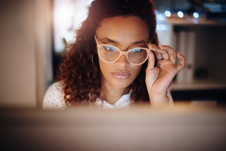 Reading, laptop and woman at night with glasses for online planning, writing proposal and research. Freelancer, remote work and person on computer for article, journalism and deadline for copywritingの写真素材