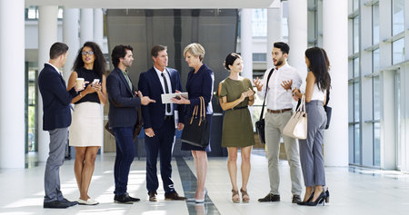 Business, people and group with talking in lobby for b2b networking, company collaboration or staff meeting. Corporate employees, diversity team or waiting for conference with discussion and planningの写真素材