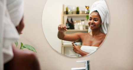 Body care, deodorant and woman with spray in mirror for odor control, fresh smell or getting ready in bathroom. Reflection, person or grooming routine in home for underarm hygiene and clean fragranceの写真素材