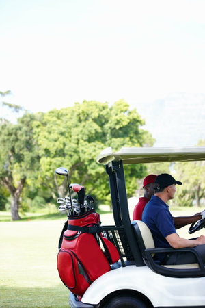 Friends, bag and driving golf cart on outdoor field for search of ball, club and male people for sport or fitness. Man, athlete and side view of vehicle for moving on green grass for exercise.の写真素材