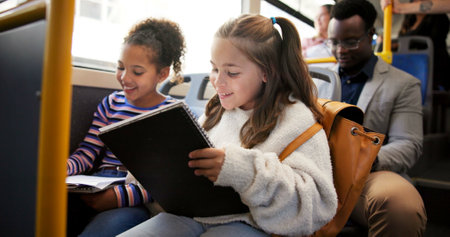 Travel, children and writing in book on bus for homework assessment, studying or educational project. Friends, girls and riding on public transport with exam learning, school destination or commutingの写真素材