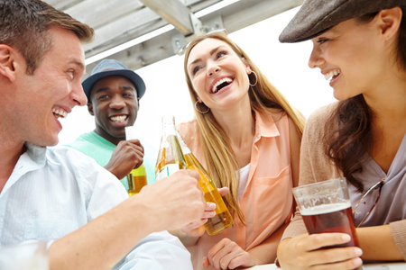 Beer, funny and group of people at pub together for hang out, reunion or social gathering. Alcohol, friends or smile with men and women laughing at restaurant for bonding, conversation or jokingの写真素材