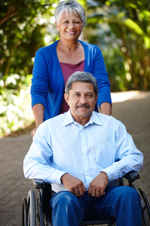 Portrait, support and wheelchair with senior couple outdoor in garden of home together for bonding. Assistance, medical or healthcare and person with disability in backyard for fresh air or walkの写真素材