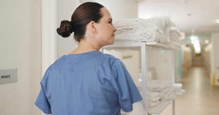 Woman, nurse and healthcare with cart in hospital with cleaning, hygiene and medical supplies for patient care at retirement clinic. Professional, caregiver and hall with sanitary towels for healthの写真素材