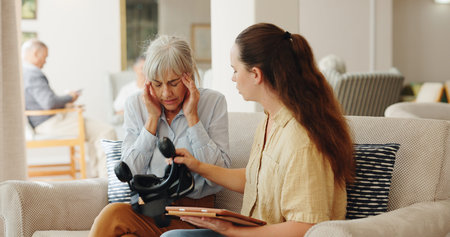 Senior woman, headache and virtual reality on couch with tablet for test, metaverse and caregiver in retirement home. Geriatric psychiatrist, ar vision and tired with pain in exam for dementia on appの写真素材