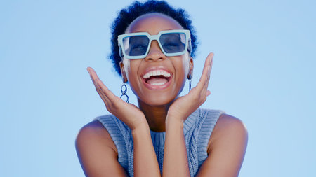 Black woman, sunglasses and face in studio with happy, excited and fashion creativity by blue...