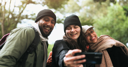Friends, happy selfie and hiking adventure in nature together, man and women in forest for outdoor travel. Photography, smile and group of people relax on camping trip with trees, hug and memory.の写真素材