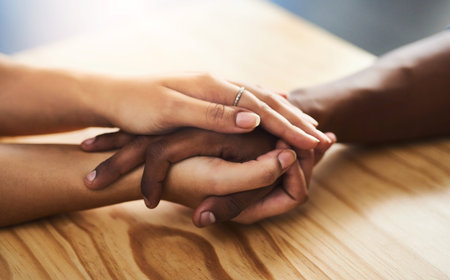 Interracial couple, hands and empathy with support for relationship, commitment or trust at home. Closeup, people or touch with sympathy for confession, love or respect on wooden table at houseの写真素材