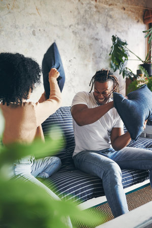 Sofa, couple and playful with pillow fight in home, bonding together and healthy dating with game. House, woman and man with cushion for relationship, connection or having fun on couch in living roomの写真素材